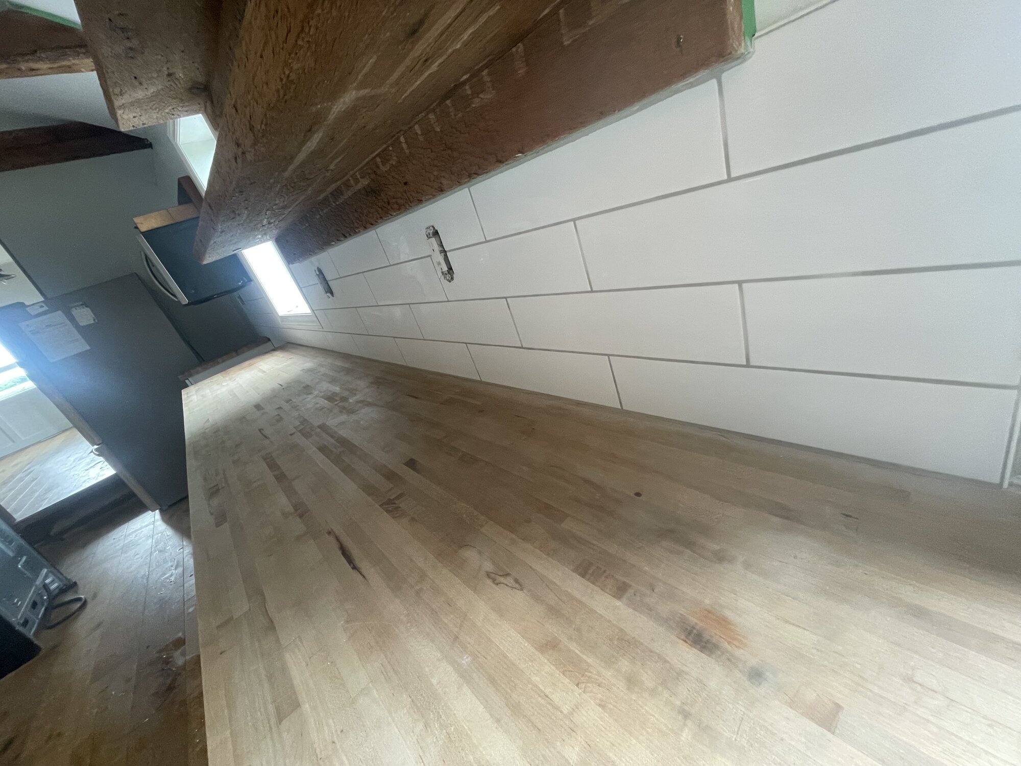 Large white tile laid along the same wall above the butcher block counter.