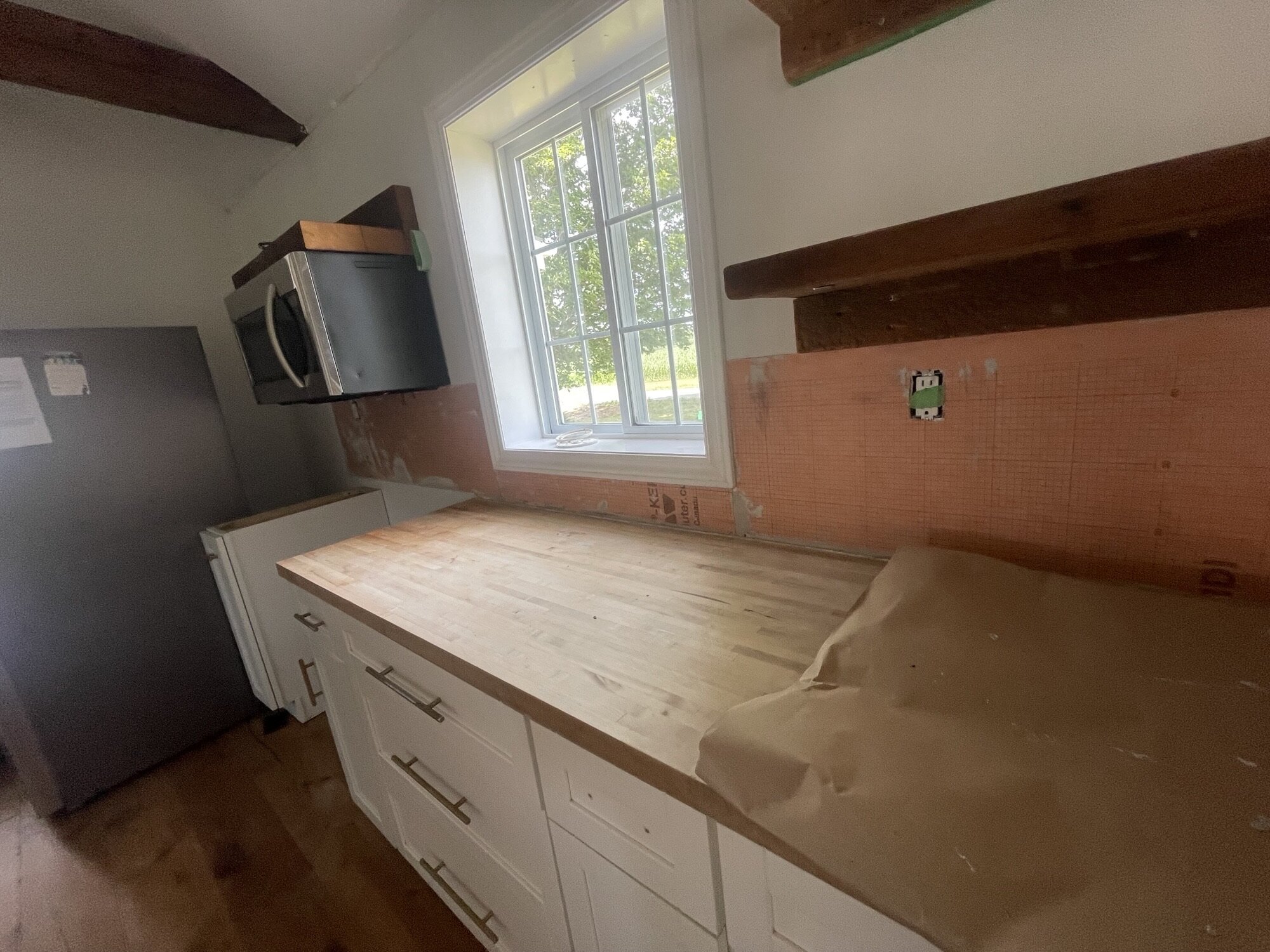 A kitchen wall of bare orange backer board above a butcher block counter.