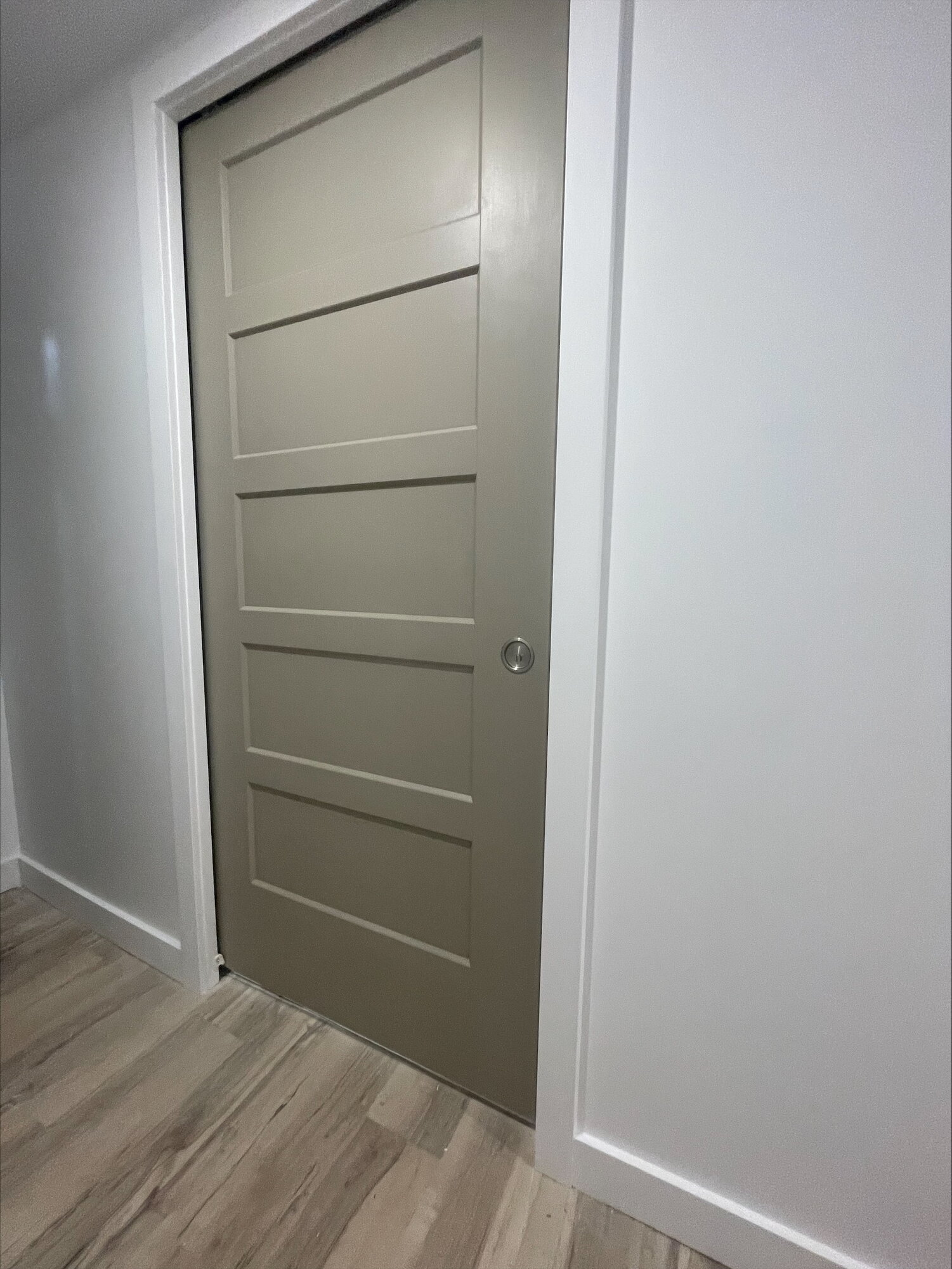 A grey five panel door in a white cased doorway, above a plank floor.