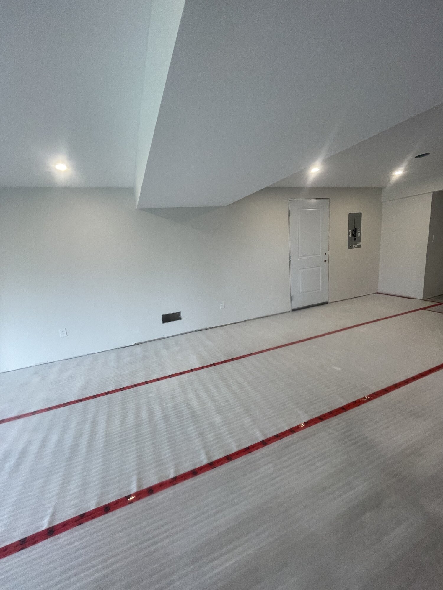 A basement room with pot lights and underlay rolled out across the floor.