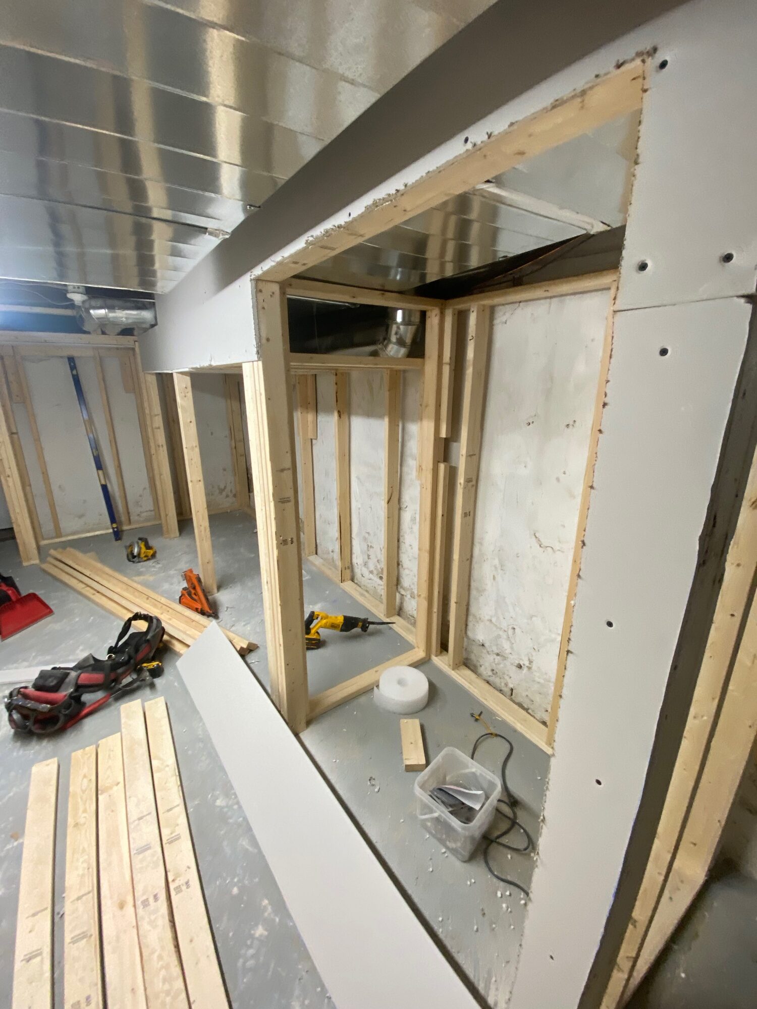 New wood stud walls framed in a basement, with drywall going up on one side.