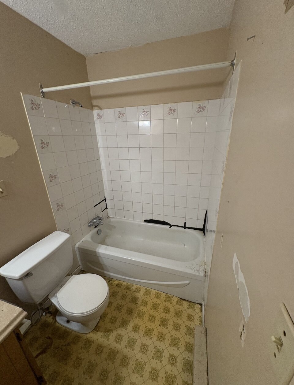 A dated bathroom with a white tile tub surround and a patterned yellow floor.