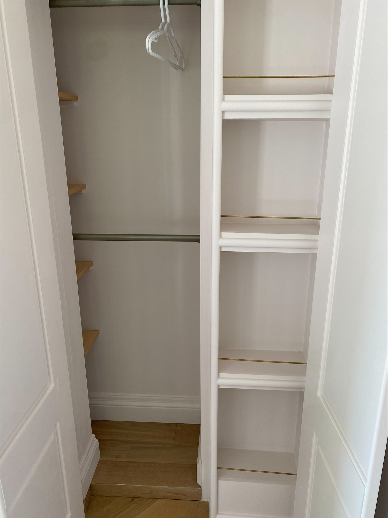 A walk in closet finished in white, with built in shelves, a hanging rod and a wood floor.
