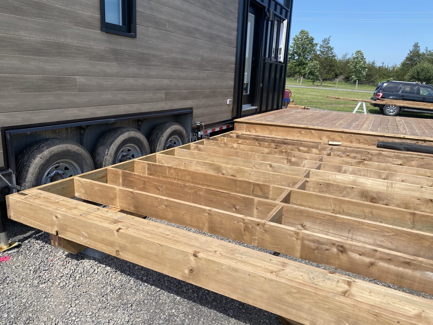 The pressure treated frame of a new deck, joists set on blocks beside a tiny home.