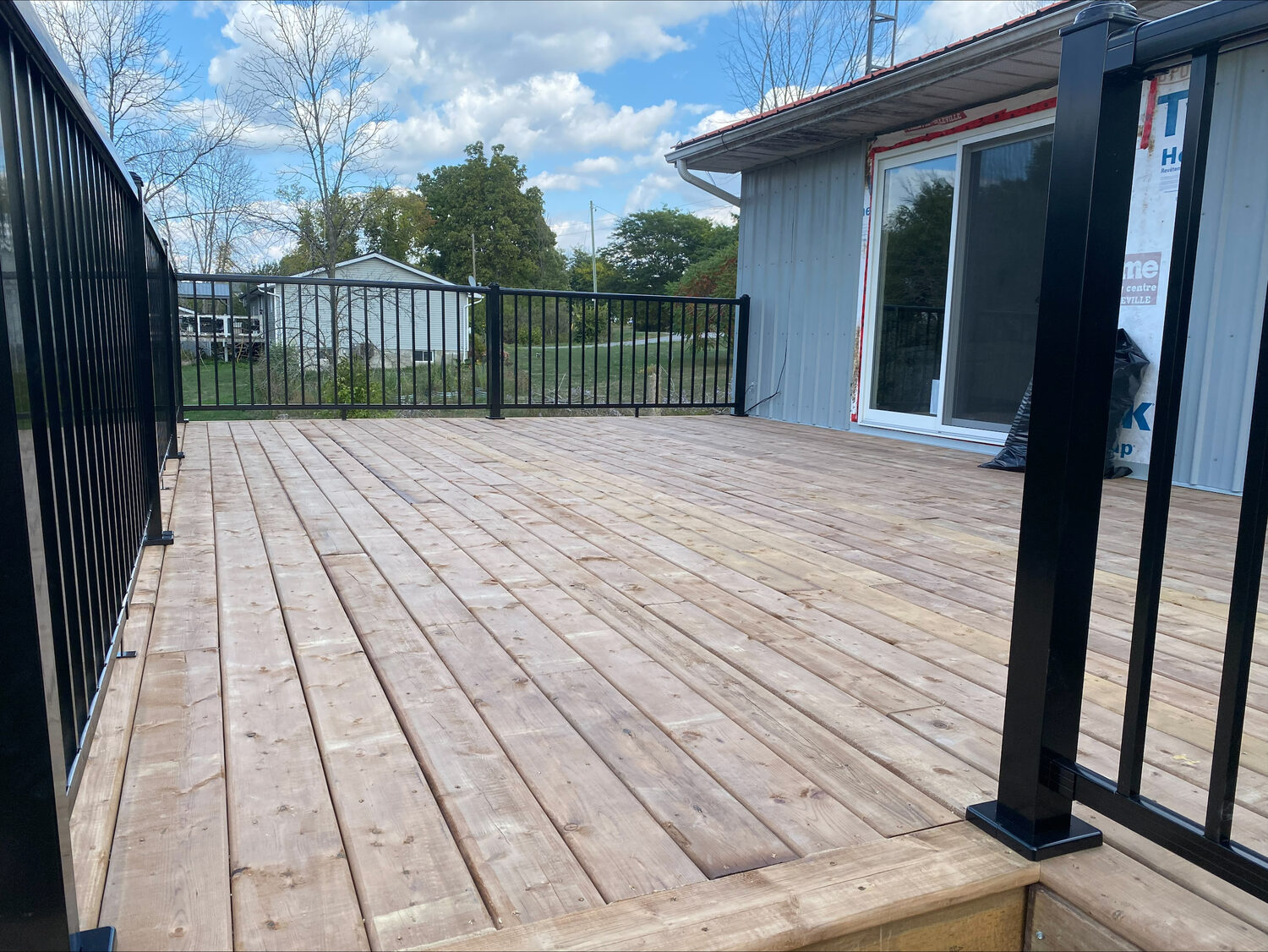 A wide new wood deck with black aluminum railing off a sliding door.