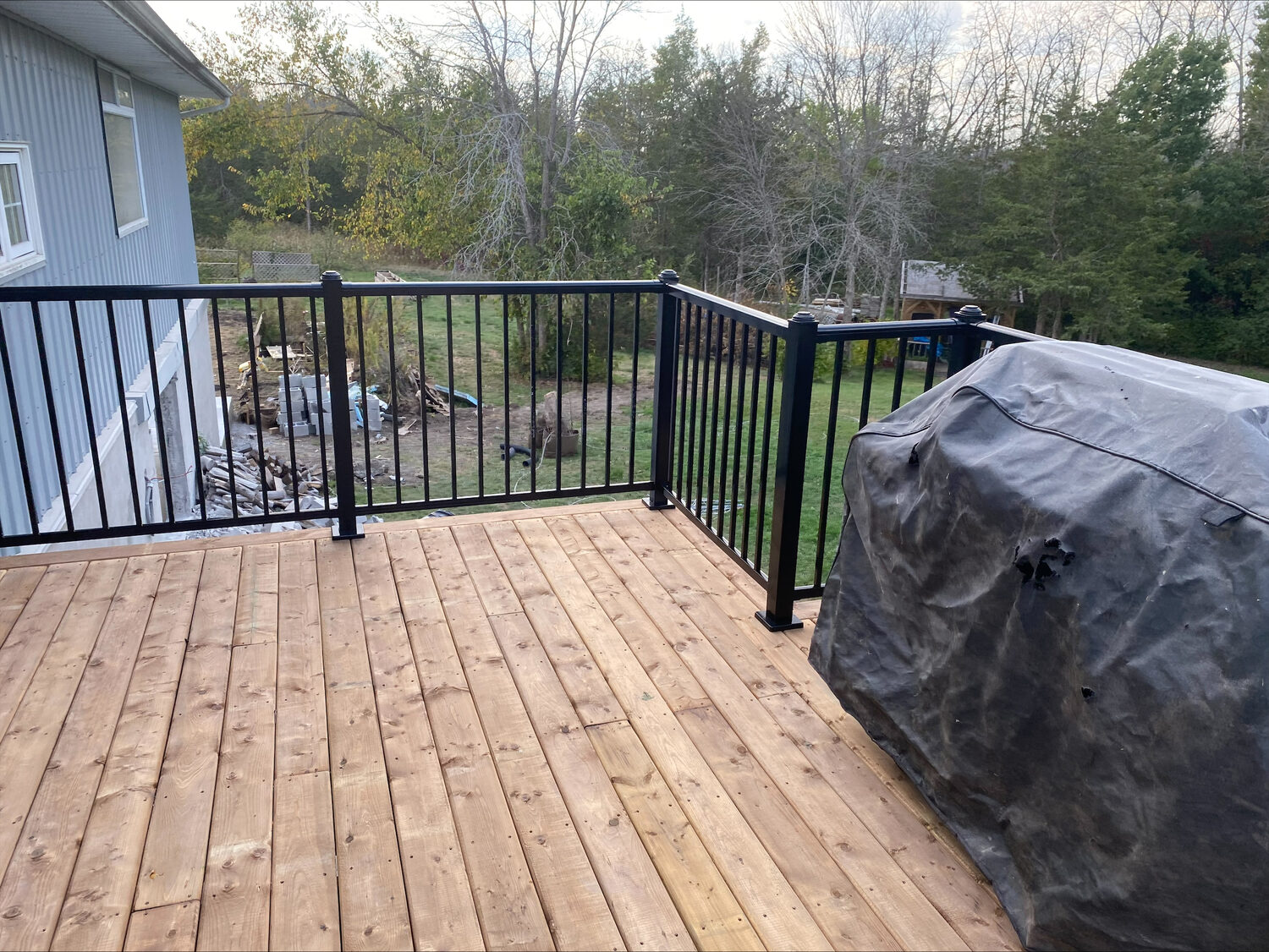 A new wood deck with black aluminum railing, looking out over a treed back yard.