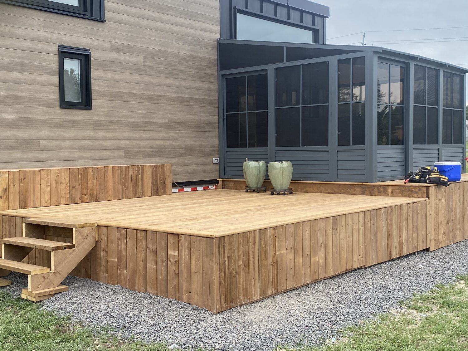 The finished deck with board skirting and steps, wrapping a tiny home and its sunroom.