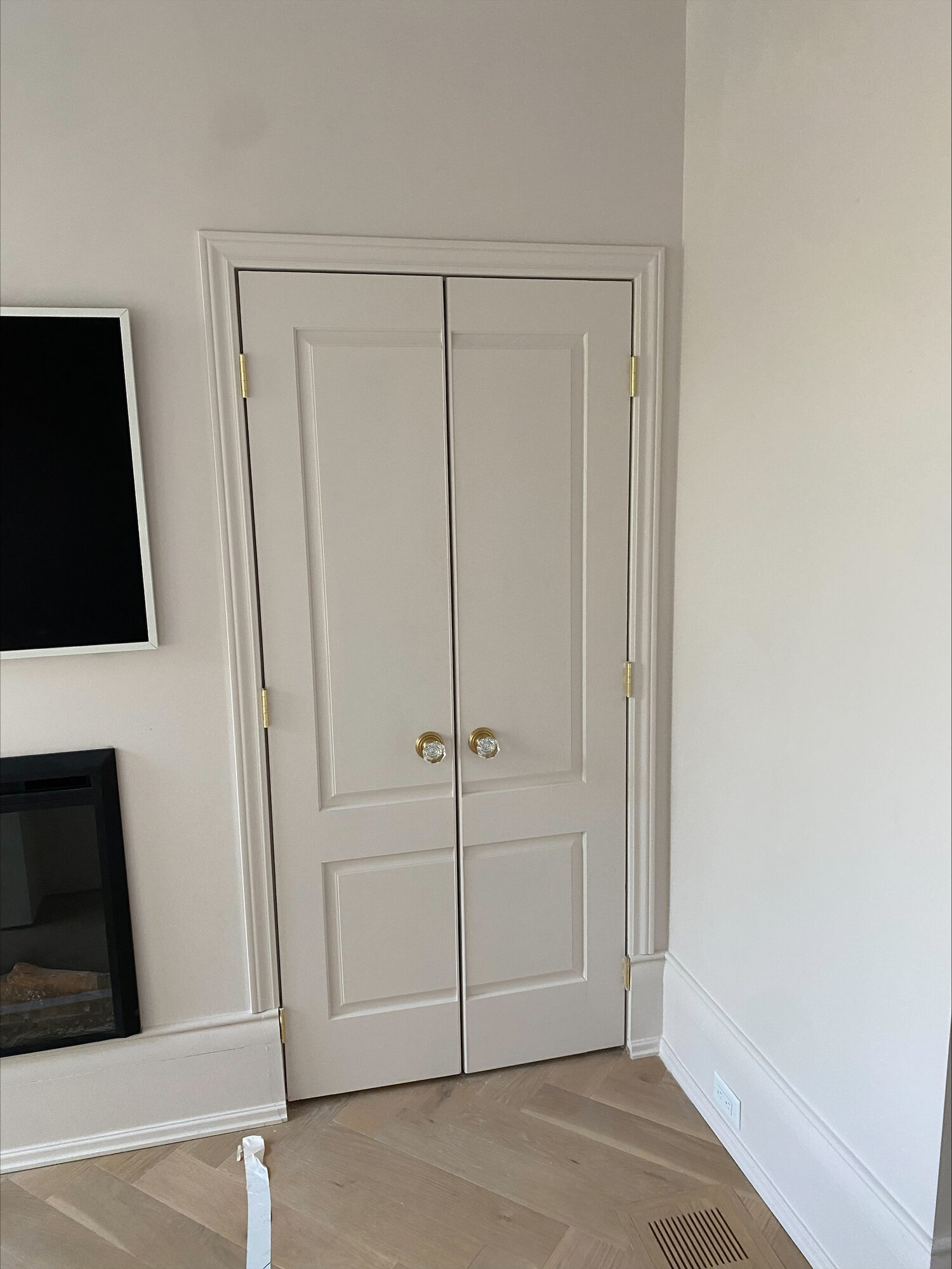 White two panel double doors with brass knobs, cased in white trim above a herringbone wood floor.