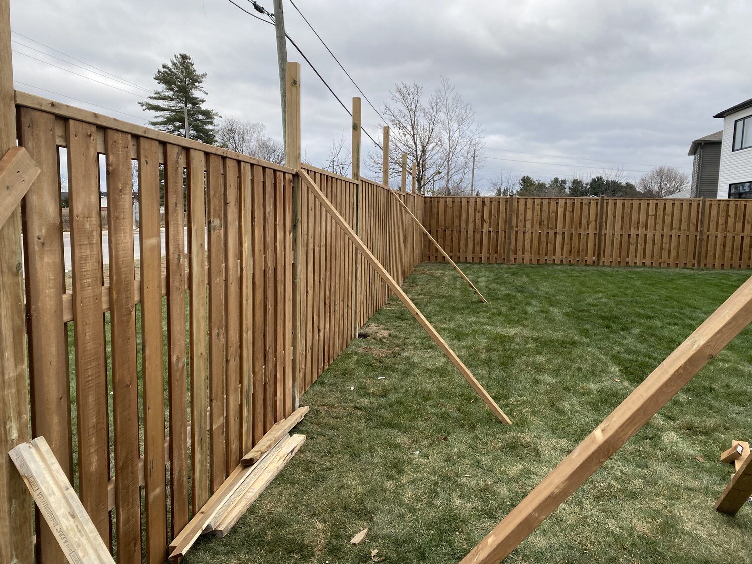 A new wood privacy fence going up around a sodded back yard, braced while the posts set.