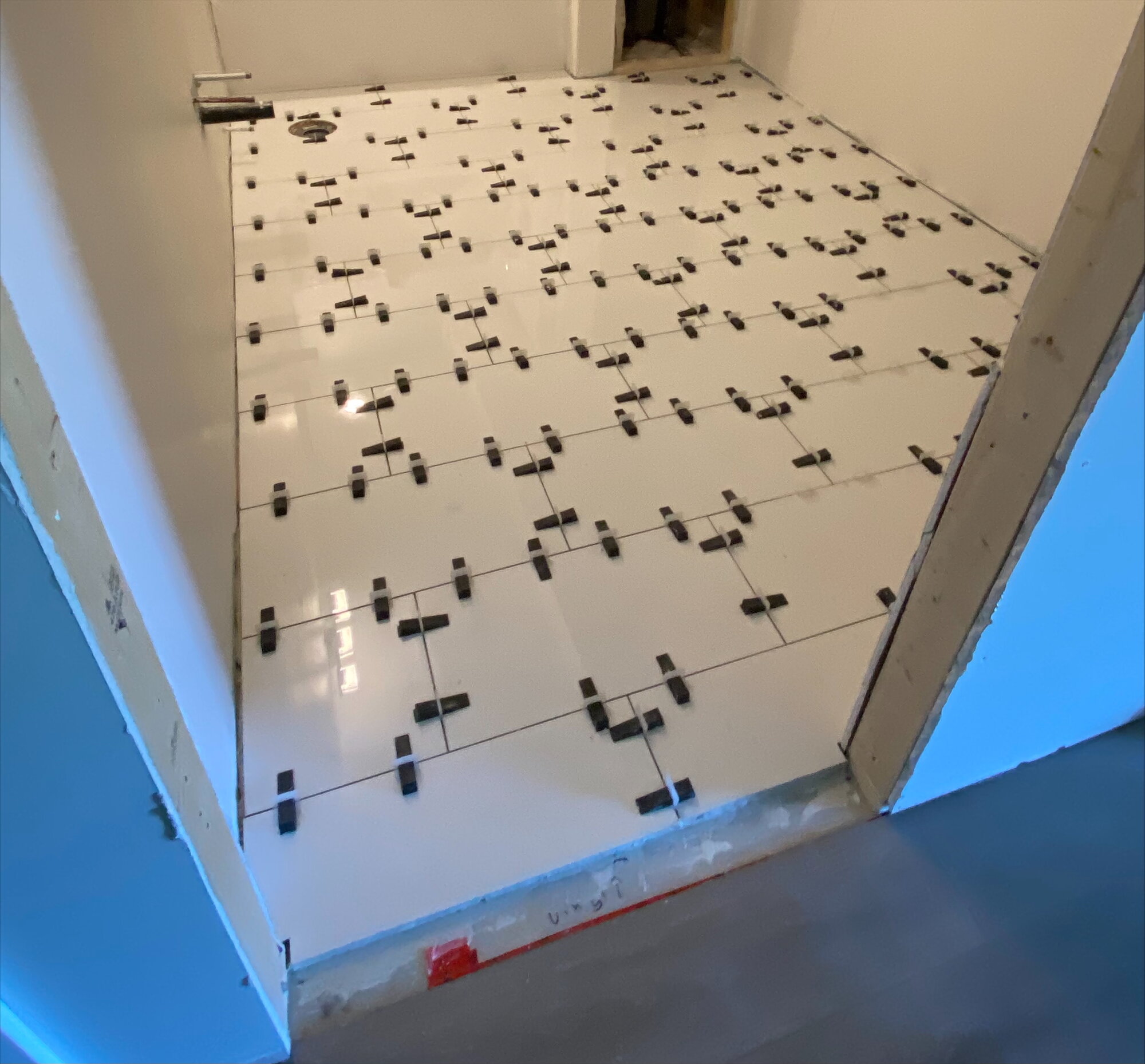 Large white floor tile being laid with levelling clips.