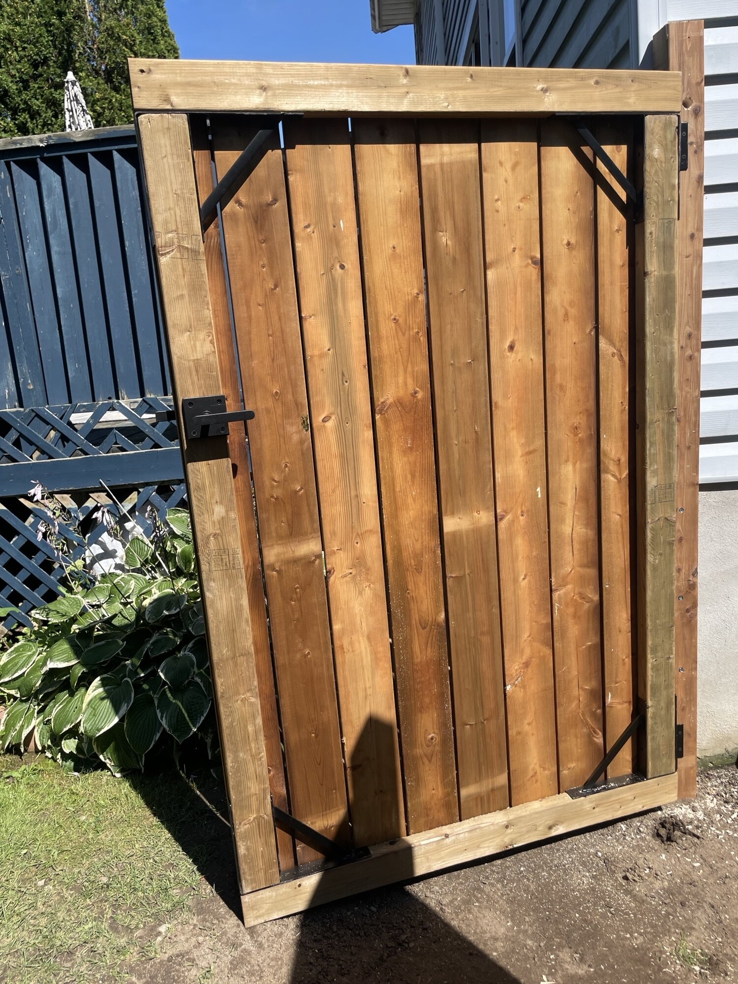 A new wood gate with black hinges and a black latch, beside a navy blue deck.
