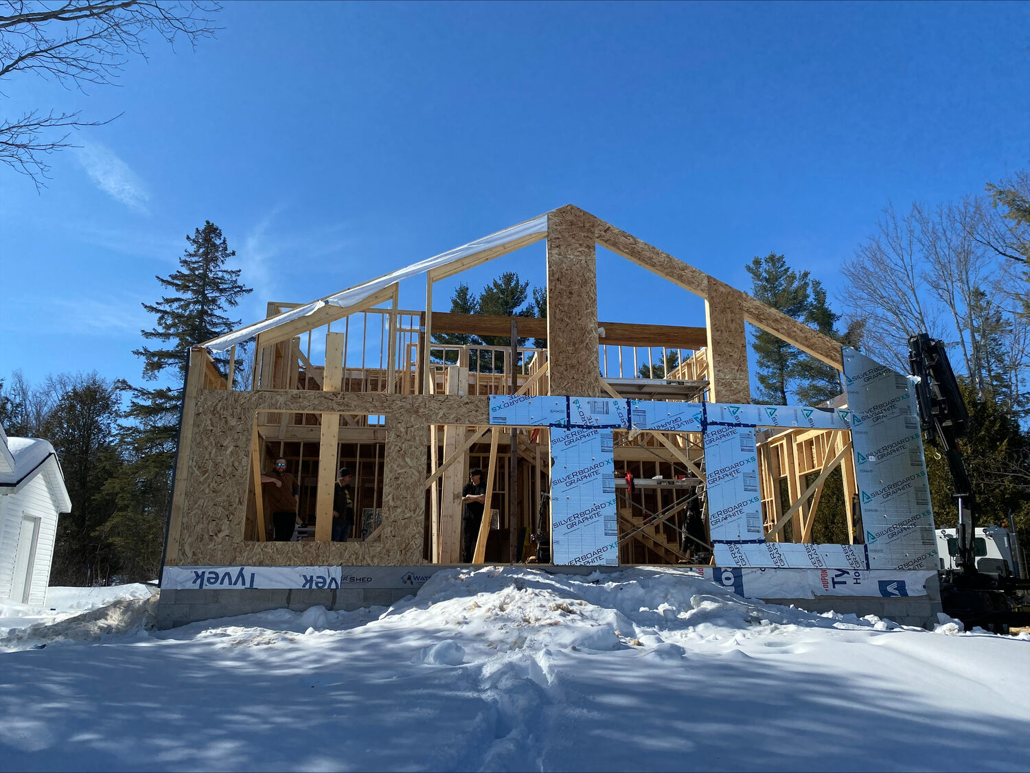 A new house framed and sheathed in winter, its gable walls standing against a blue sky over the snow.