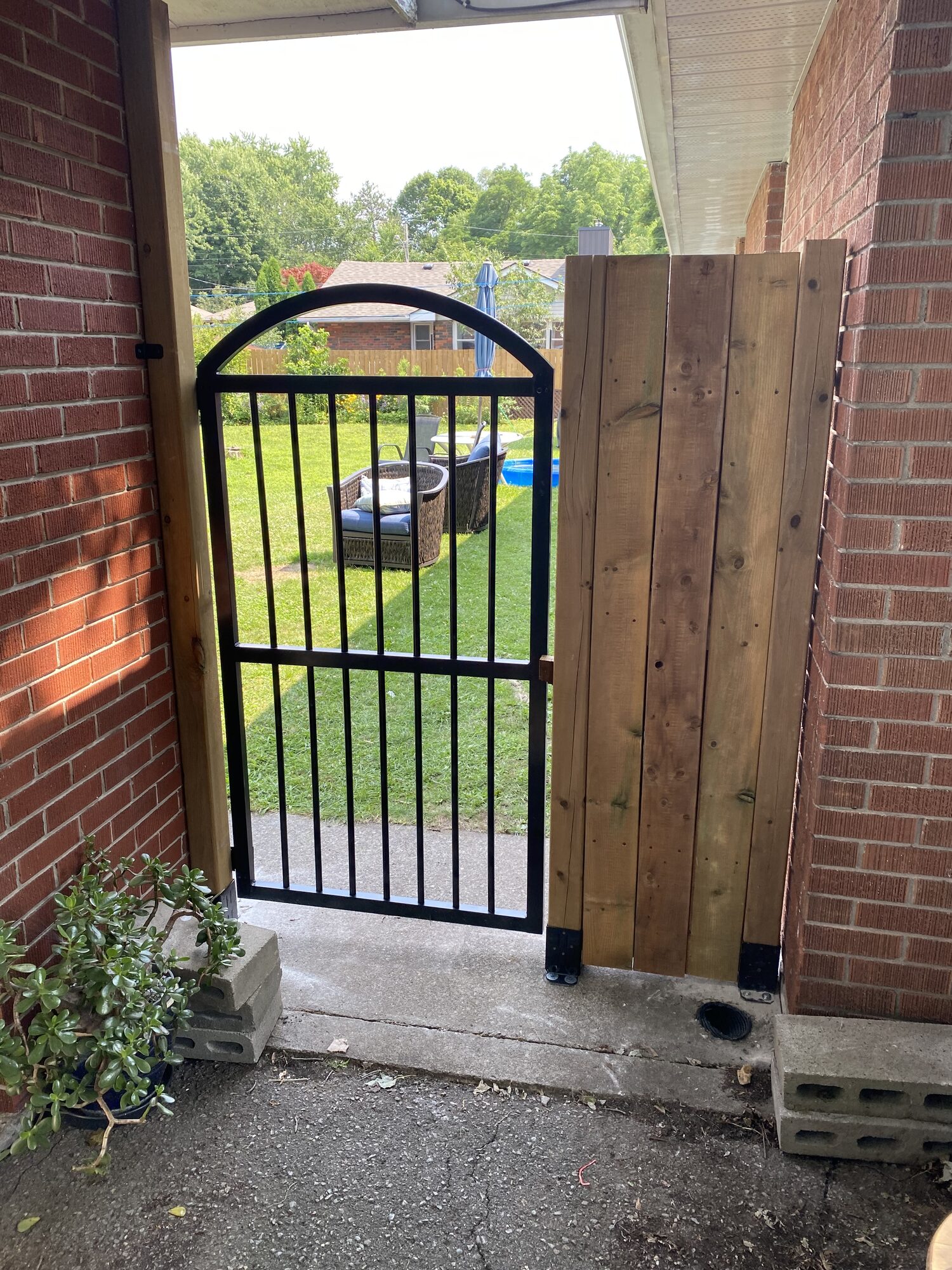 The same black arched gate seen from the patio side, hung between brick walls with a wood fence panel beside it.