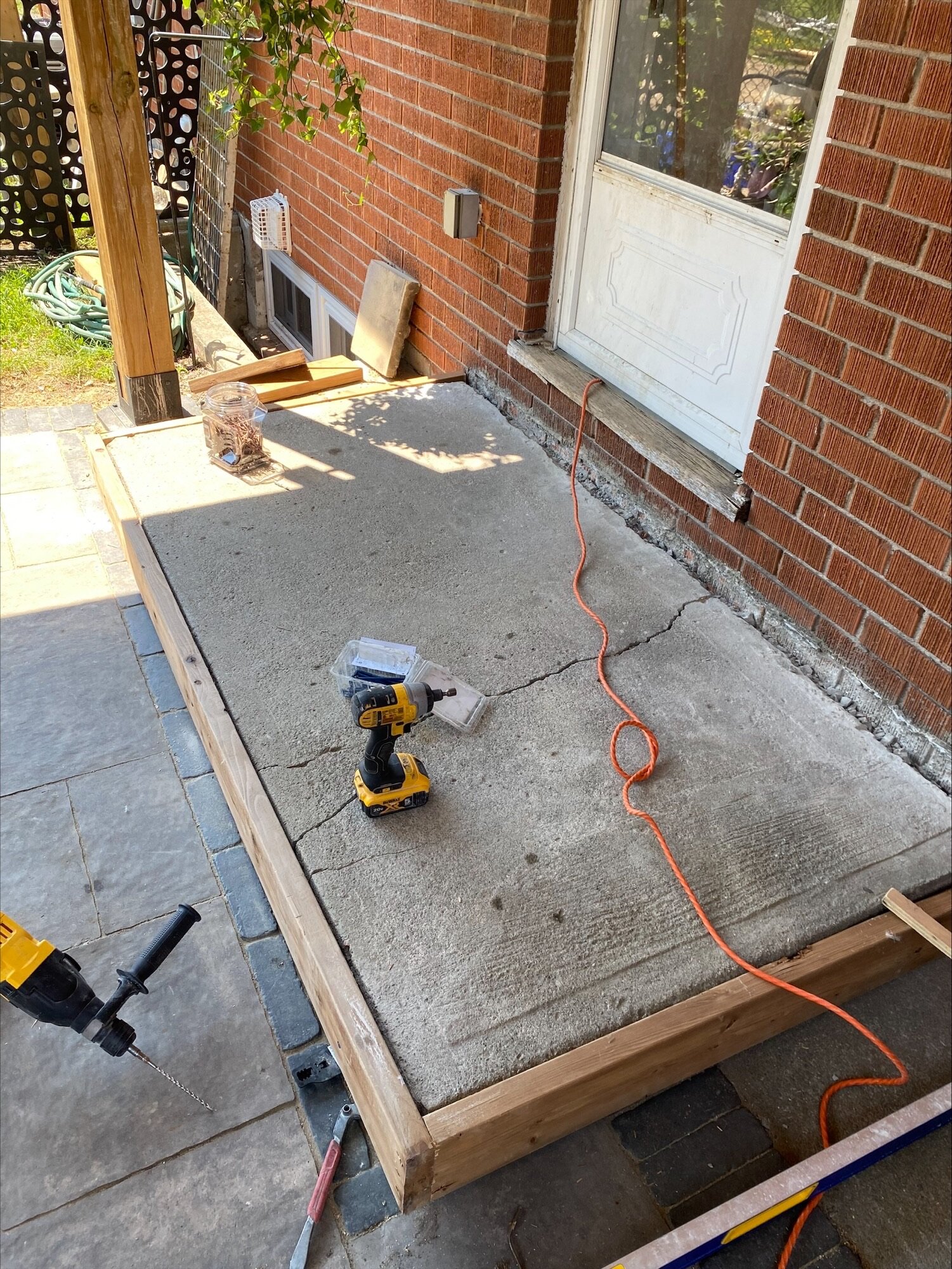 A concrete pad framed in wood at a back door, with tools on it mid job.