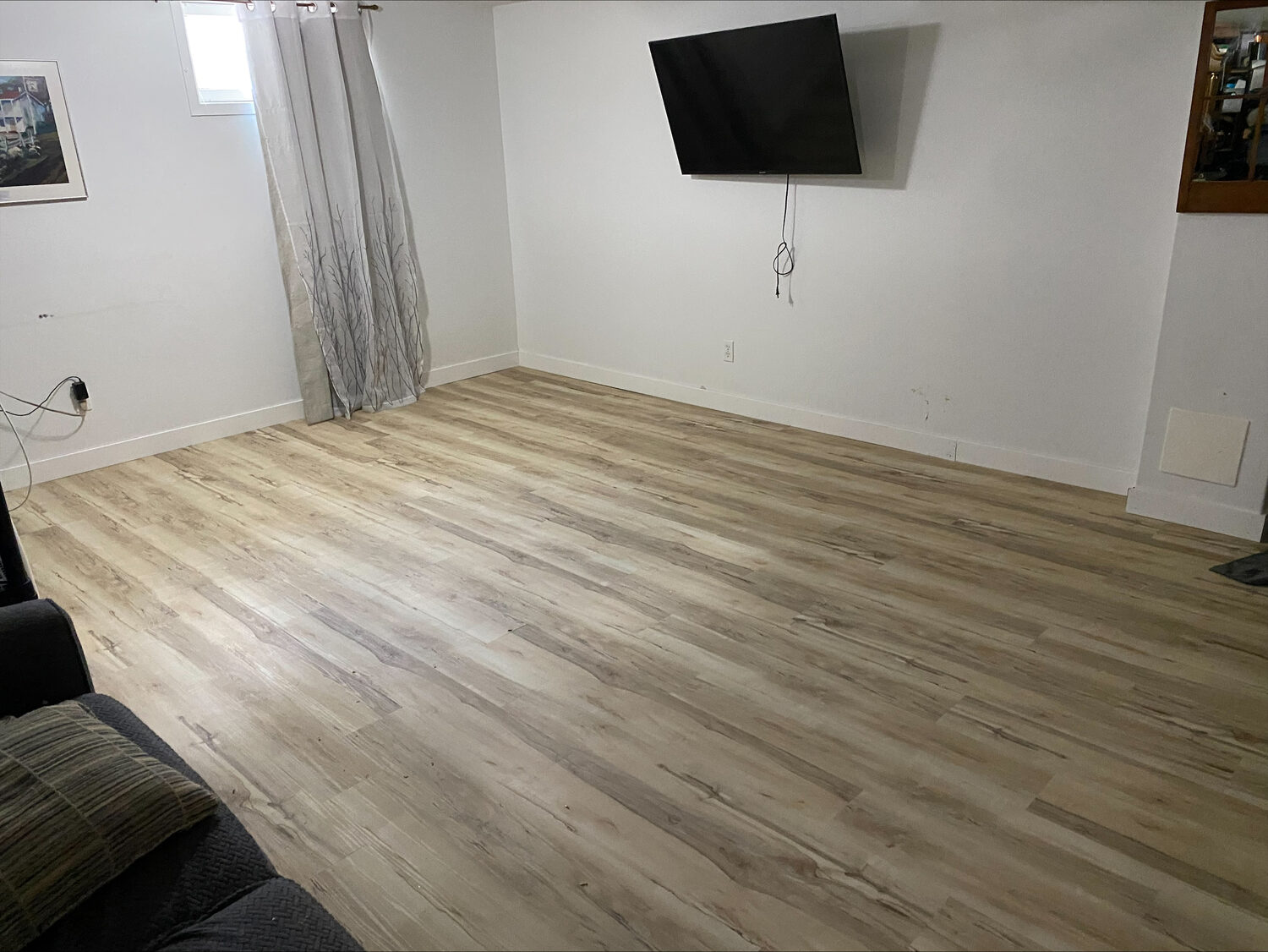 A light oak look plank floor laid across a basement room, with new white baseboard.