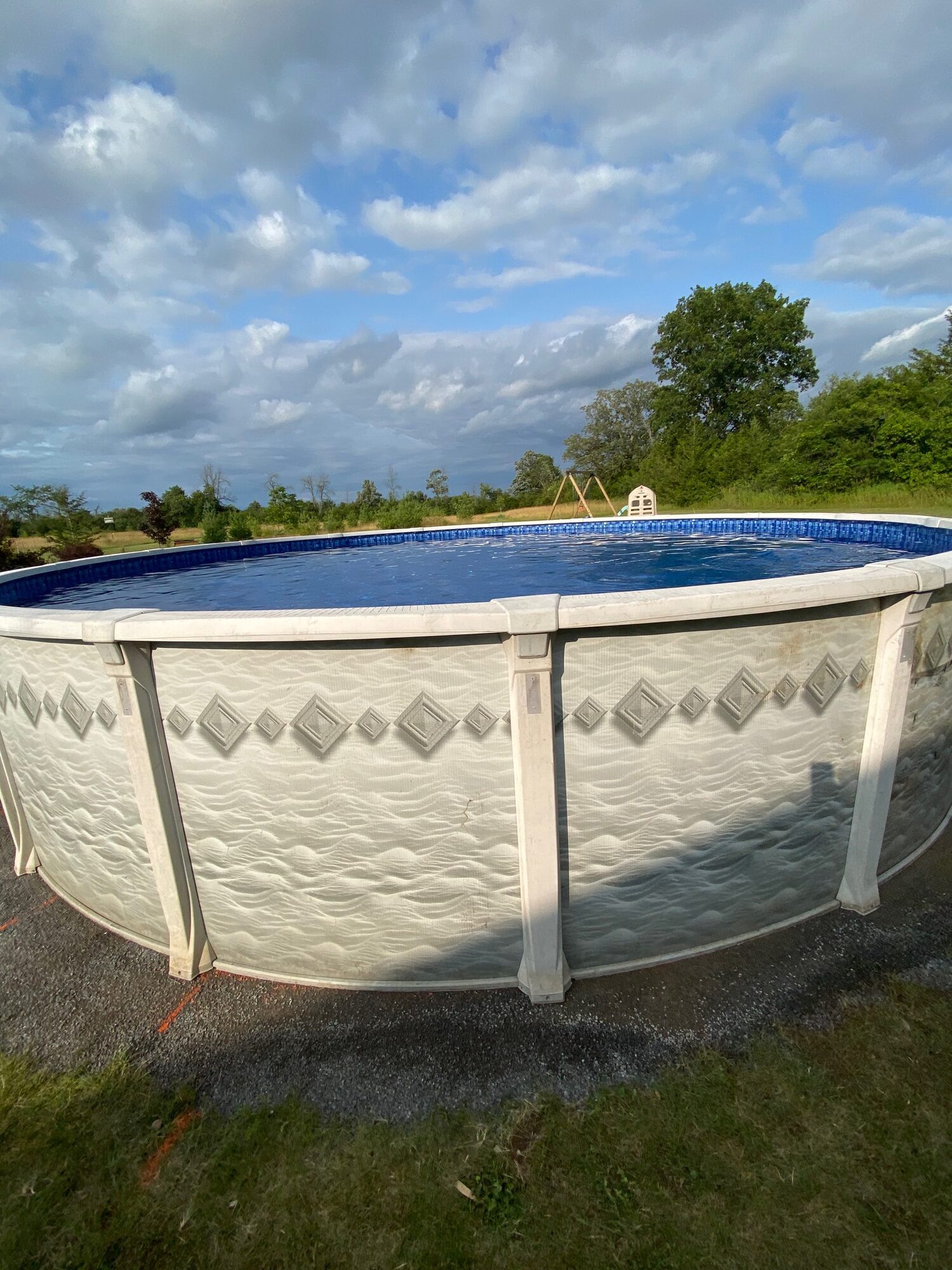 The finished above-ground pool, filled, with gravel laid around its base.