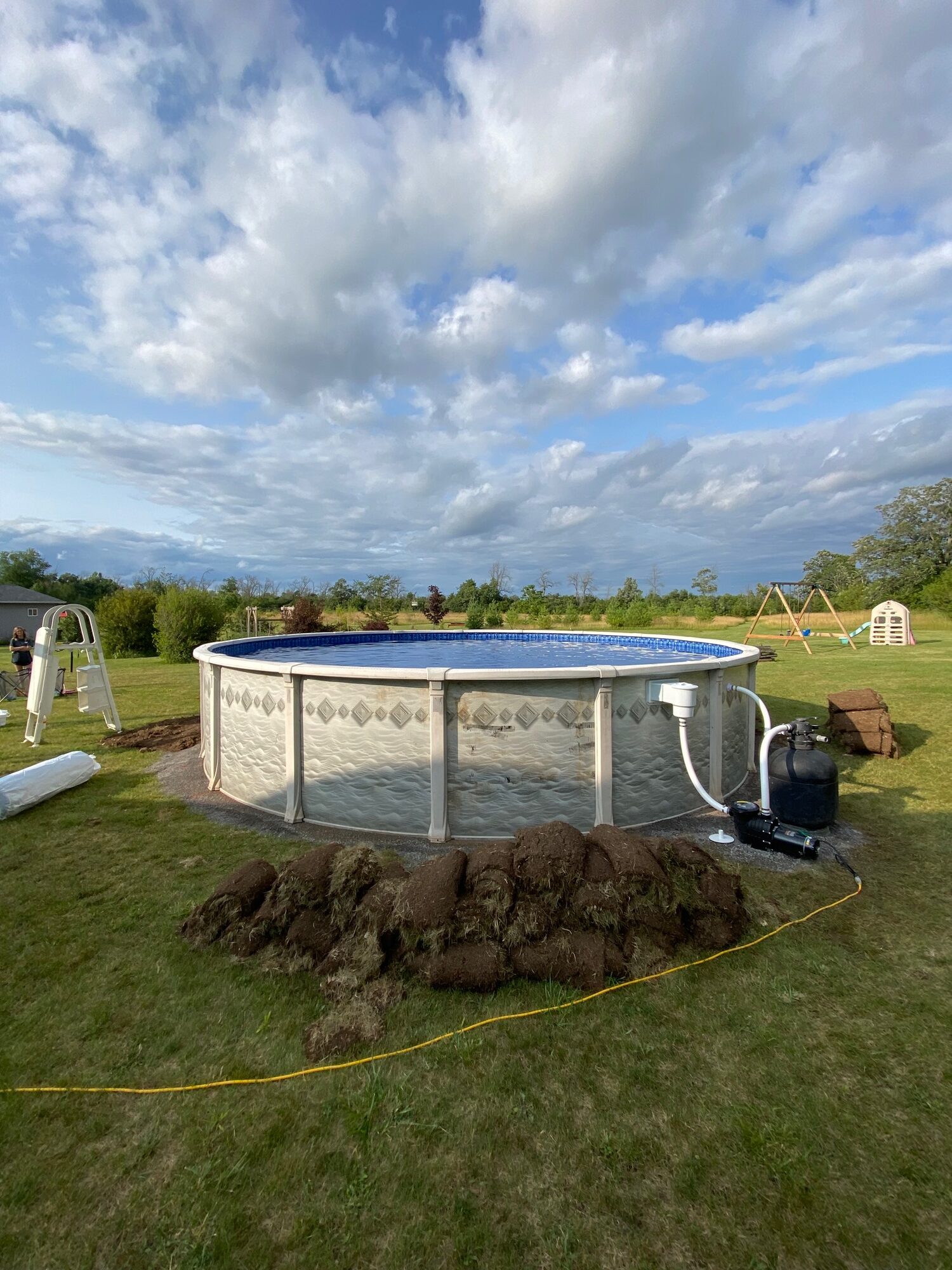 A new above-ground pool on a rural lawn, with the cut sod stacked beside it.