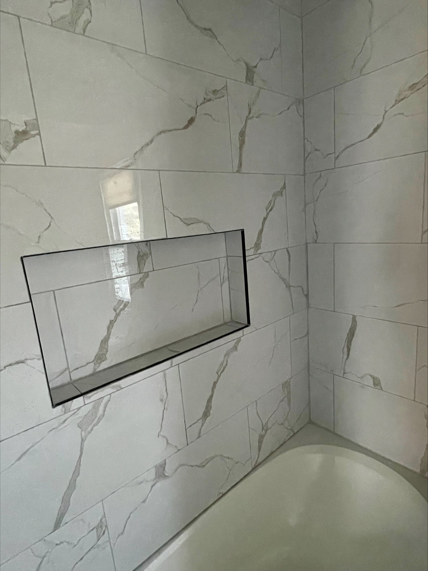 A marble look tile tub surround with a long recessed niche.