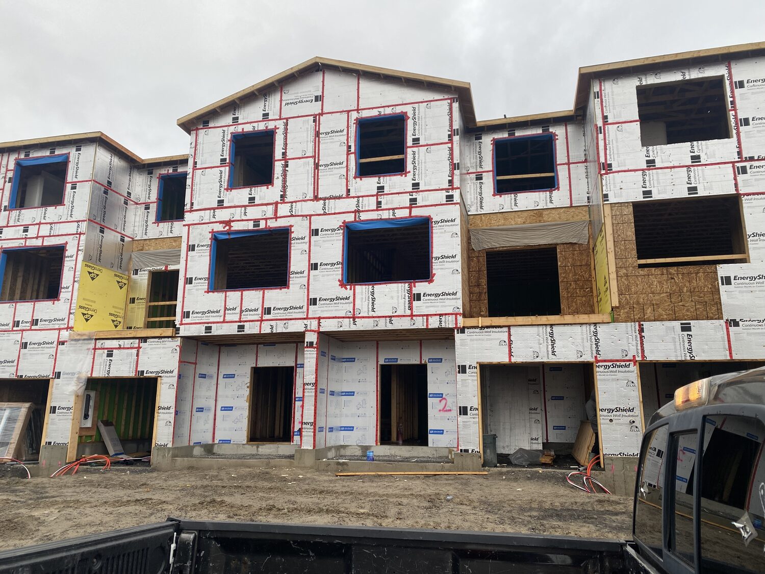 A row of three storey townhouses wrapped in rigid foam insulation board, with every seam taped, ready for siding.