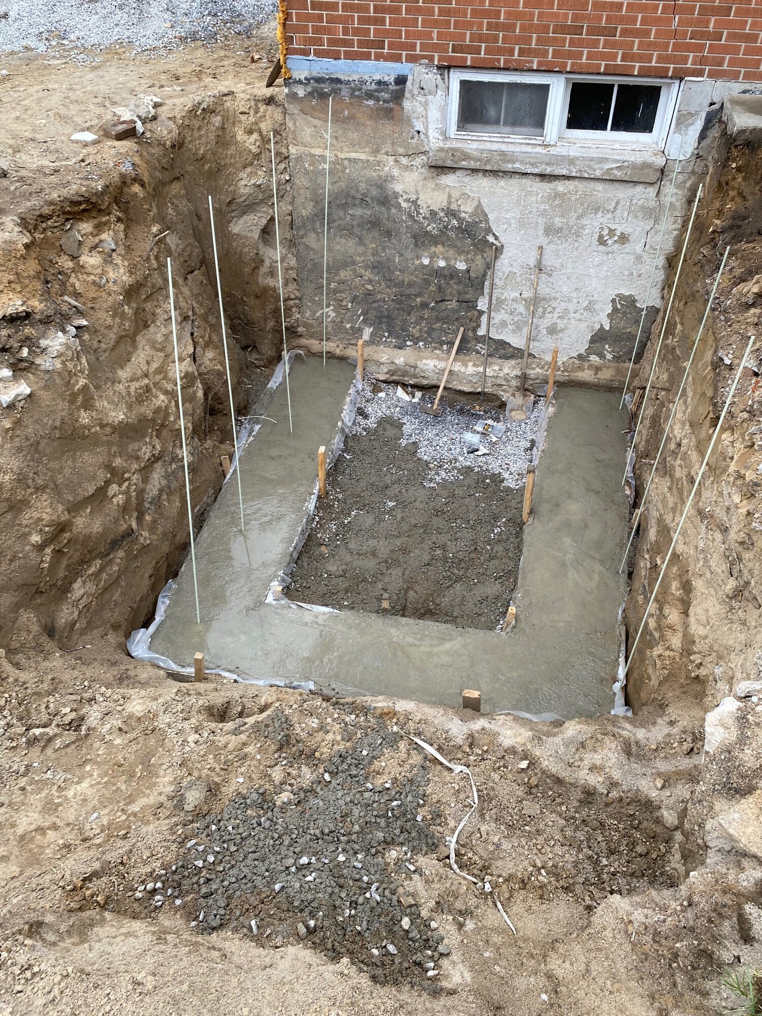 A basement wall dug out to the footing under a window, with forms set for a concrete landing.