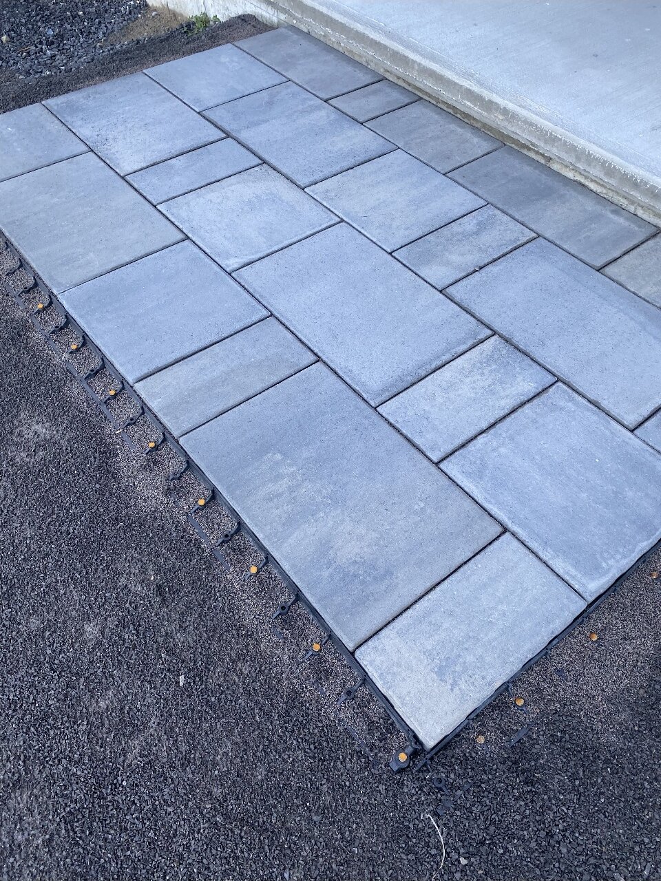 New grey paving stones laid beside a concrete step, held in place by edging set in the gravel.