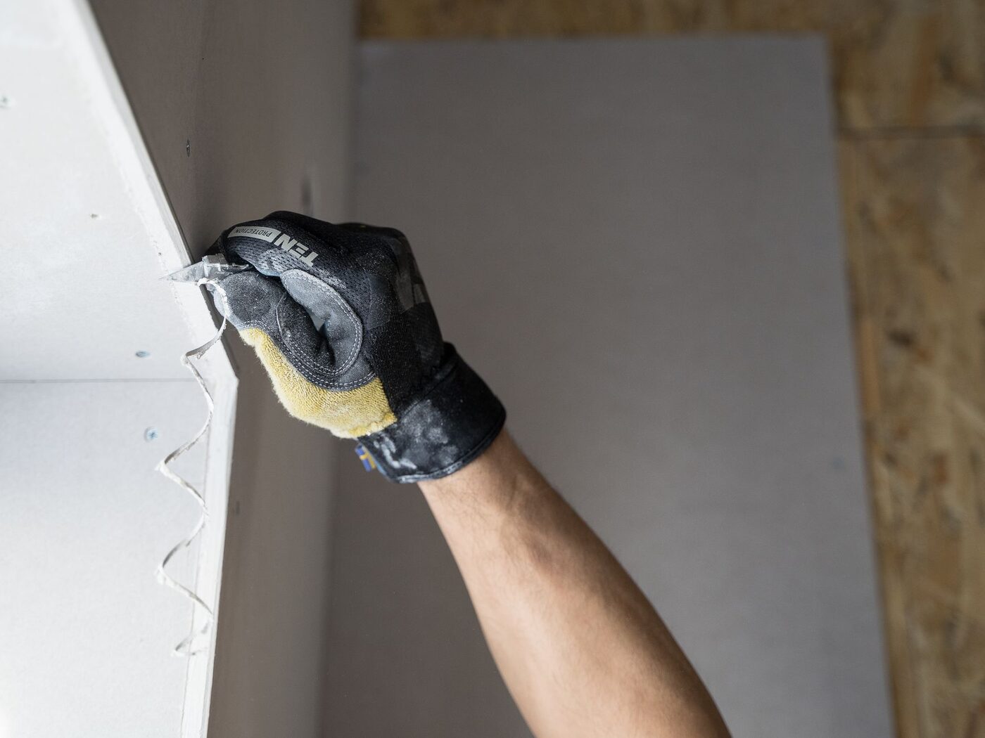 A hung drywall sheet being trimmed at a corner.