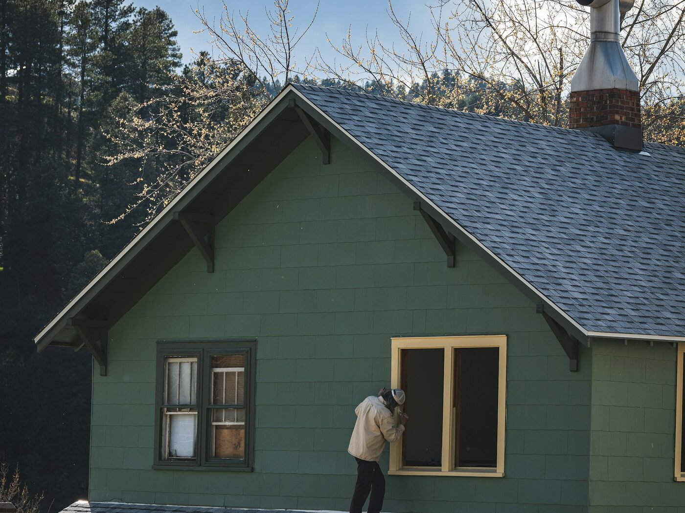 A painter brushing window trim on a shingle sided house.
