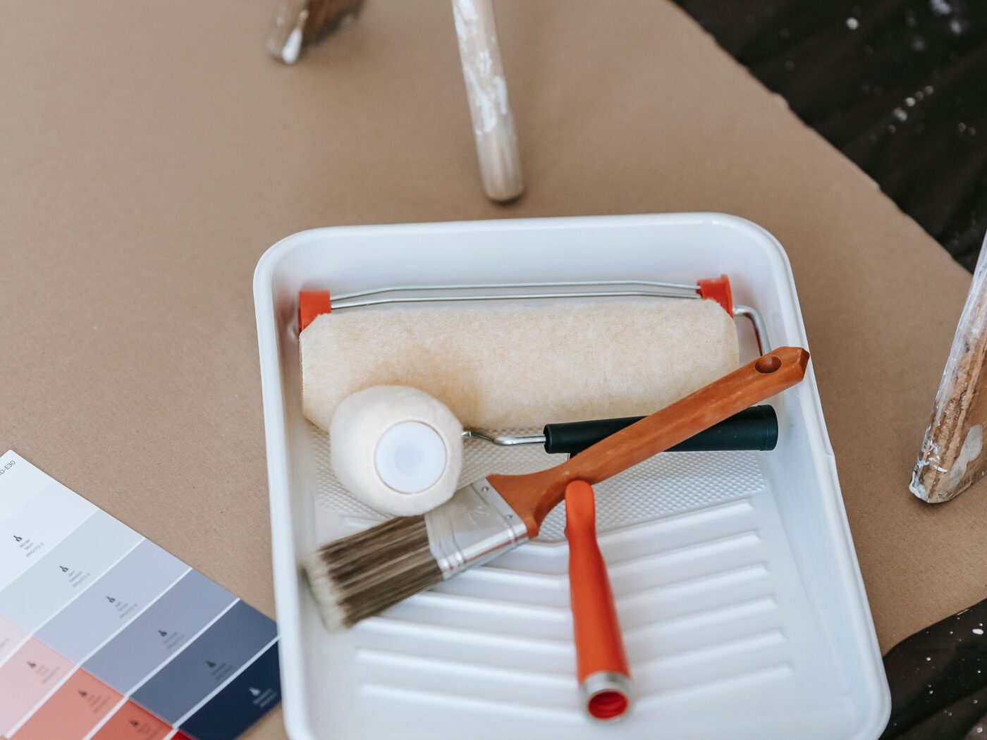A roller, a brush and a colour fan on a paint tray.